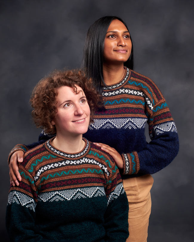 Two women dressed in matching jumpers gaze off screen.
